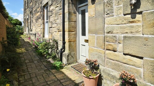 A stone building with a narrow alleyway, a door, and a window.
