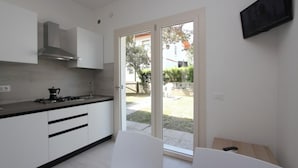 A modern kitchen with white cabinets, a gas stove, and a stainless steel range hood. There is a sliding glass door leading to an outdoor area. - Villa With Private Garden (San Michele al Tagliamento)