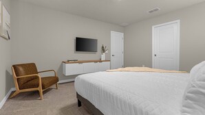 Quarto com uma cama grande, uma cadeira de madeira, uma TV fixada na parede e uma porta branca.