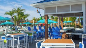 An outdoor seating area with tables and chairs, umbrellas, and palm trees. - Brand new 5 Bedroom Home Close to Disney Wl3428 (Davenport)