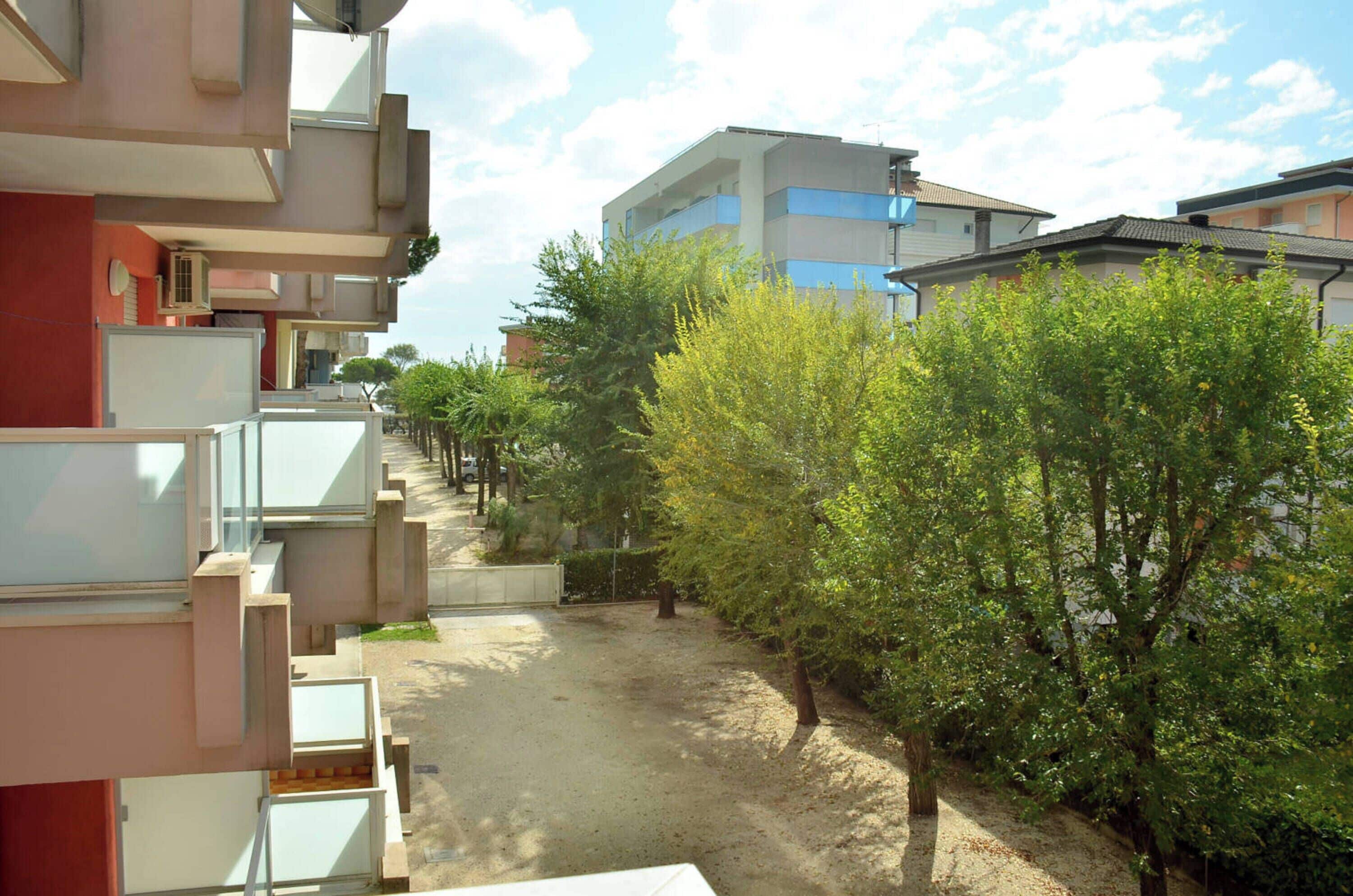 A residential area with modern buildings, a dirt path, and green trees.