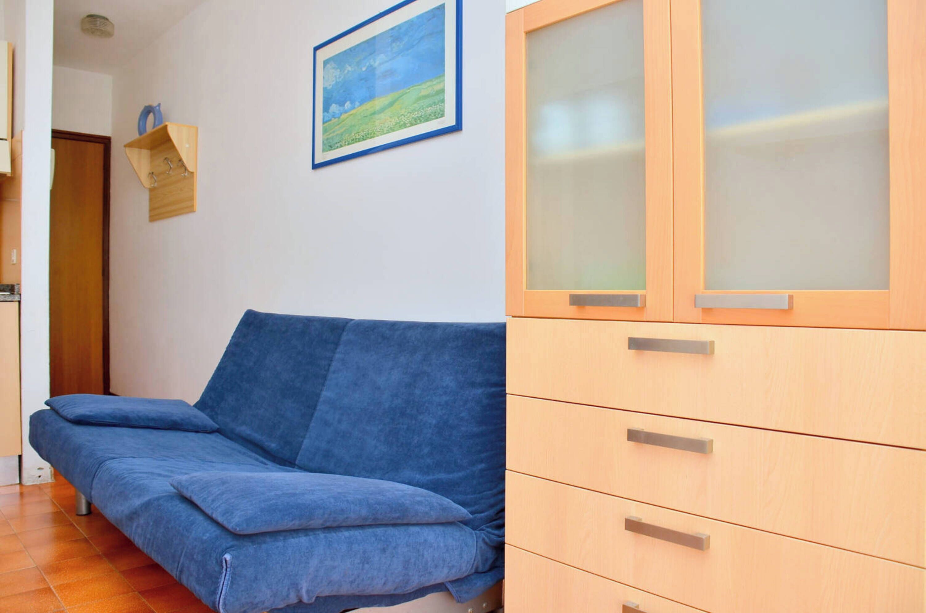 A room with a blue sofa, wooden cabinet with frosted glass doors, and a painting on the wall.