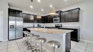 A modern kitchen with dark cabinets, stainless steel appliances, a granite countertop, and bar stools. - Cozy Home With Private Pool (Kissimmee)