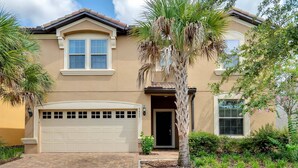 A two-story house with a beige exterior, a white garage door, and a small front porch. - Cozy Home With Private Pool (Kissimmee)