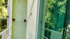 Un balcó estret amb terra de rajola, una porta de vidre i vista a vegetació verda.