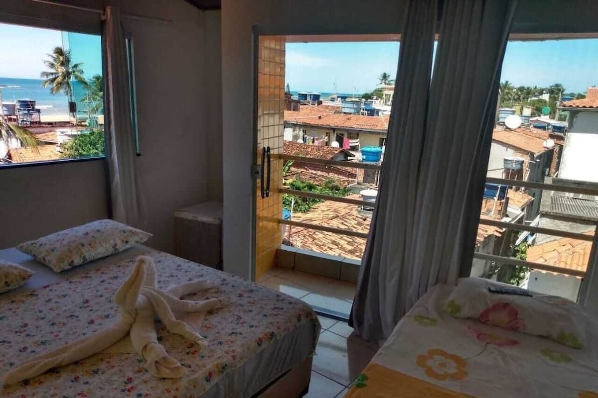 Un dormitorio con dos camas, vista a la playa y edificios desde un balcón.