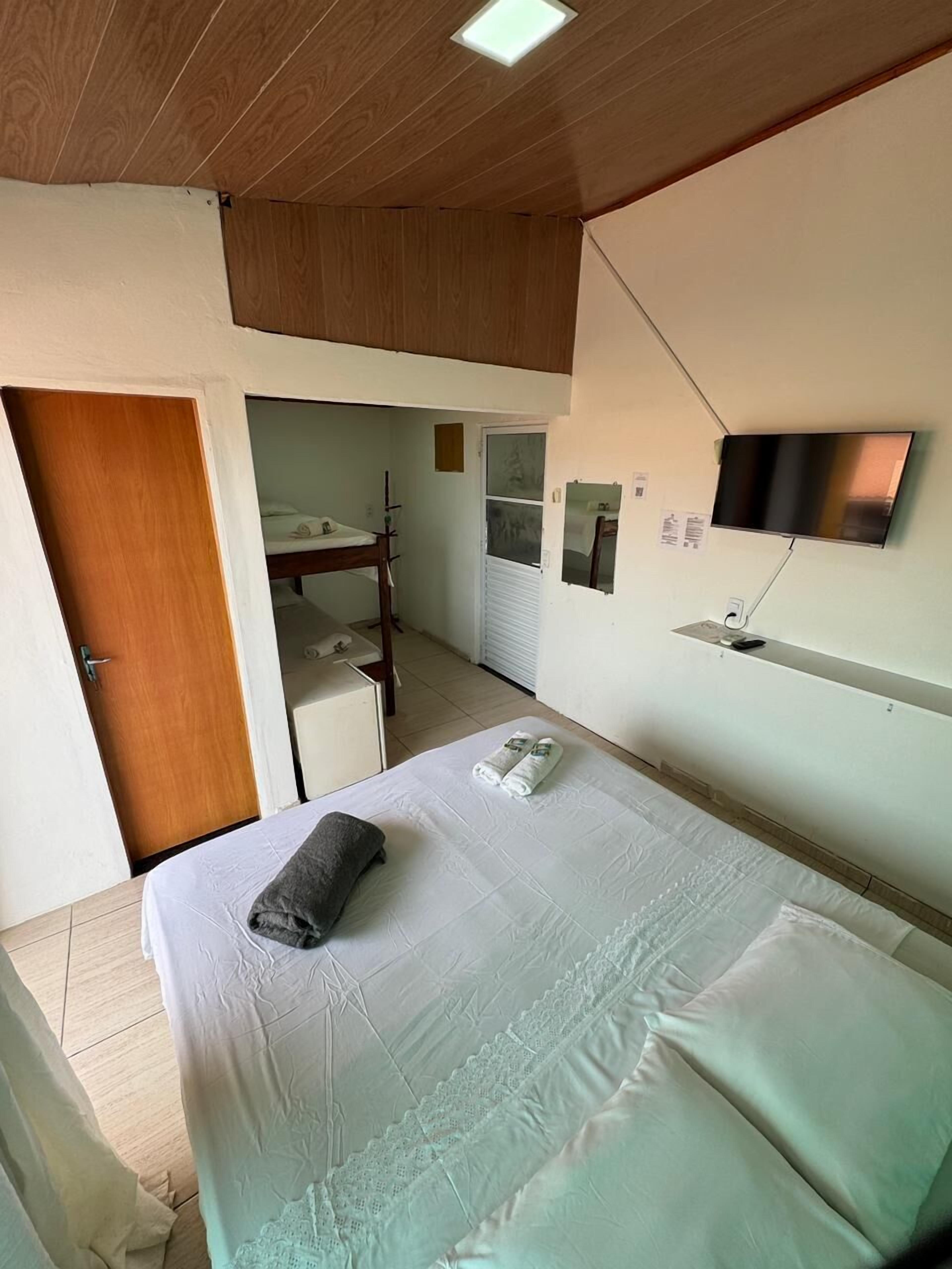 A bedroom with a bed, a wooden door, a mirror, a TV, and a small desk.