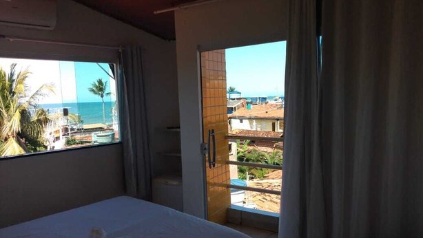 Habitació d'hotel amb un llit, una finestra amb vista al mar i un balcó amb vista a edificis i palmeres.