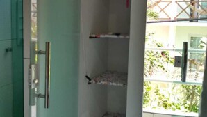 Habitació amb un bany a l'esquerra, un armari verd, una petita estanteria i vista a un balcó amb plantes.