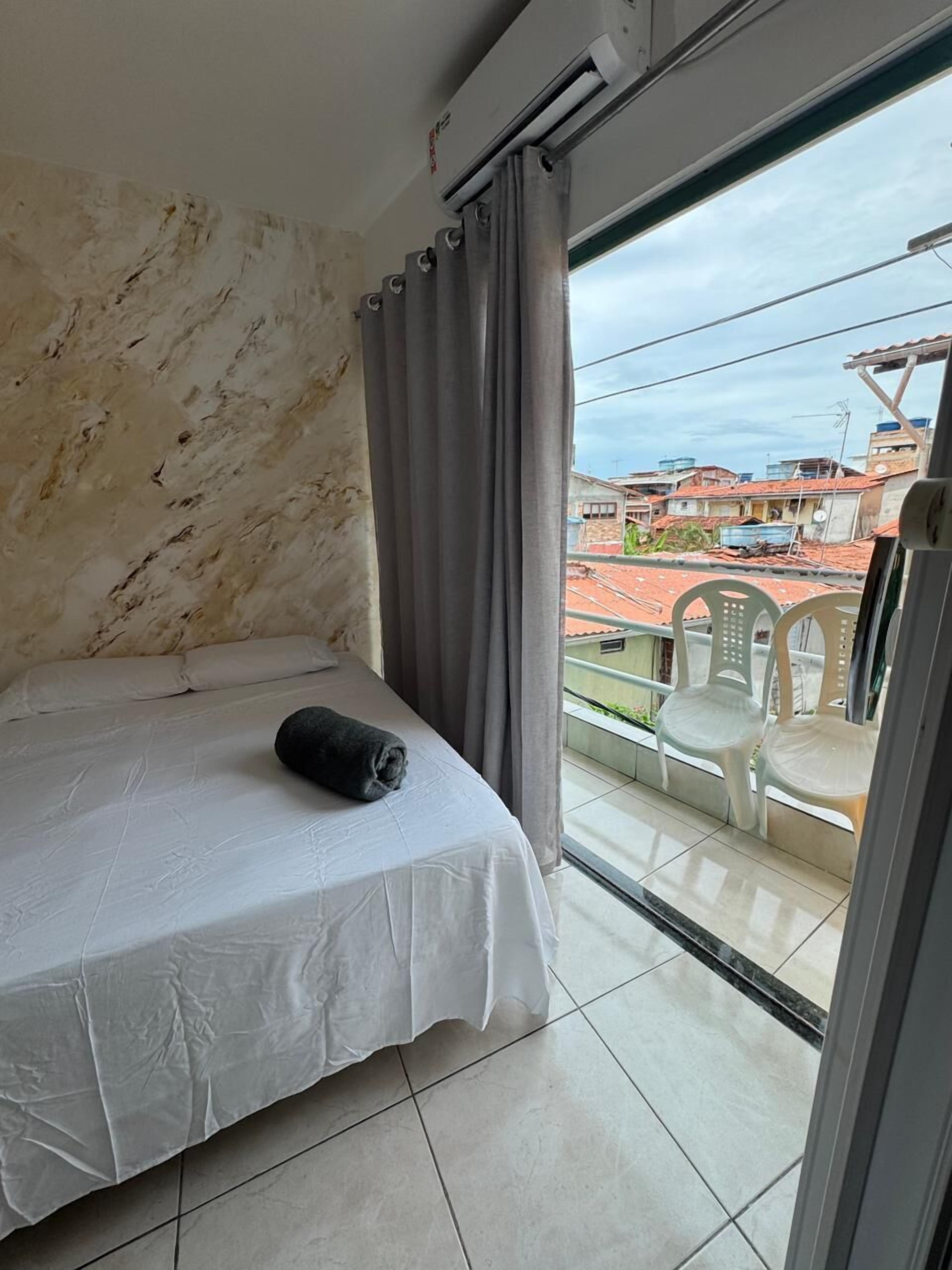 A bedroom with a bed, a window with curtains, and a view of buildings outside.