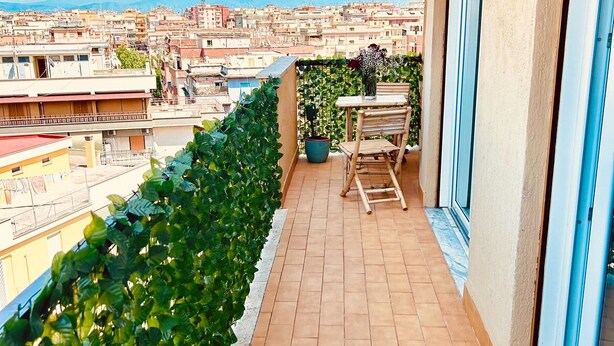 Un balcón con vistas a un paisaje urbano, una planta en maceta y una mesa con sillas.