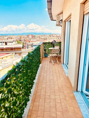 A balcony with a view of a cityscape, a potted plant, and a table with chairs. - Historic Penthouse in Rome. Ideal for business travels or tourists. (Roma)
