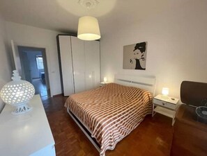 Een slaapkamer met een bed, nachtkastjes, een lamp, een kledingkast en een schilderij aan de muur.