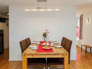 Un coin repas avec une table en bois dressée pour deux personnes, un vase rempli de fleurs et un set de table rouge.