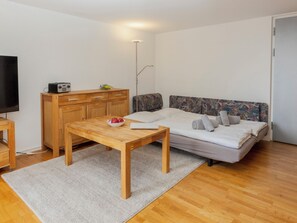Ein kleines, modernes Schlafzimmer mit Bett, Holztablett, Fernseher und einer Couch.