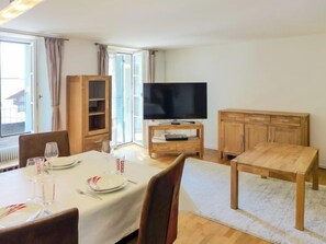 Ein Essbereich mit Tisch für zwei Personen, einem Fernseher auf einem Schrank, Holzschränken und Blick durch eine Glastür.