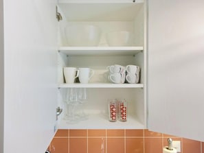 Een keuken met witte planken waarop bekers, glazen en een rol keukenpapier staan.