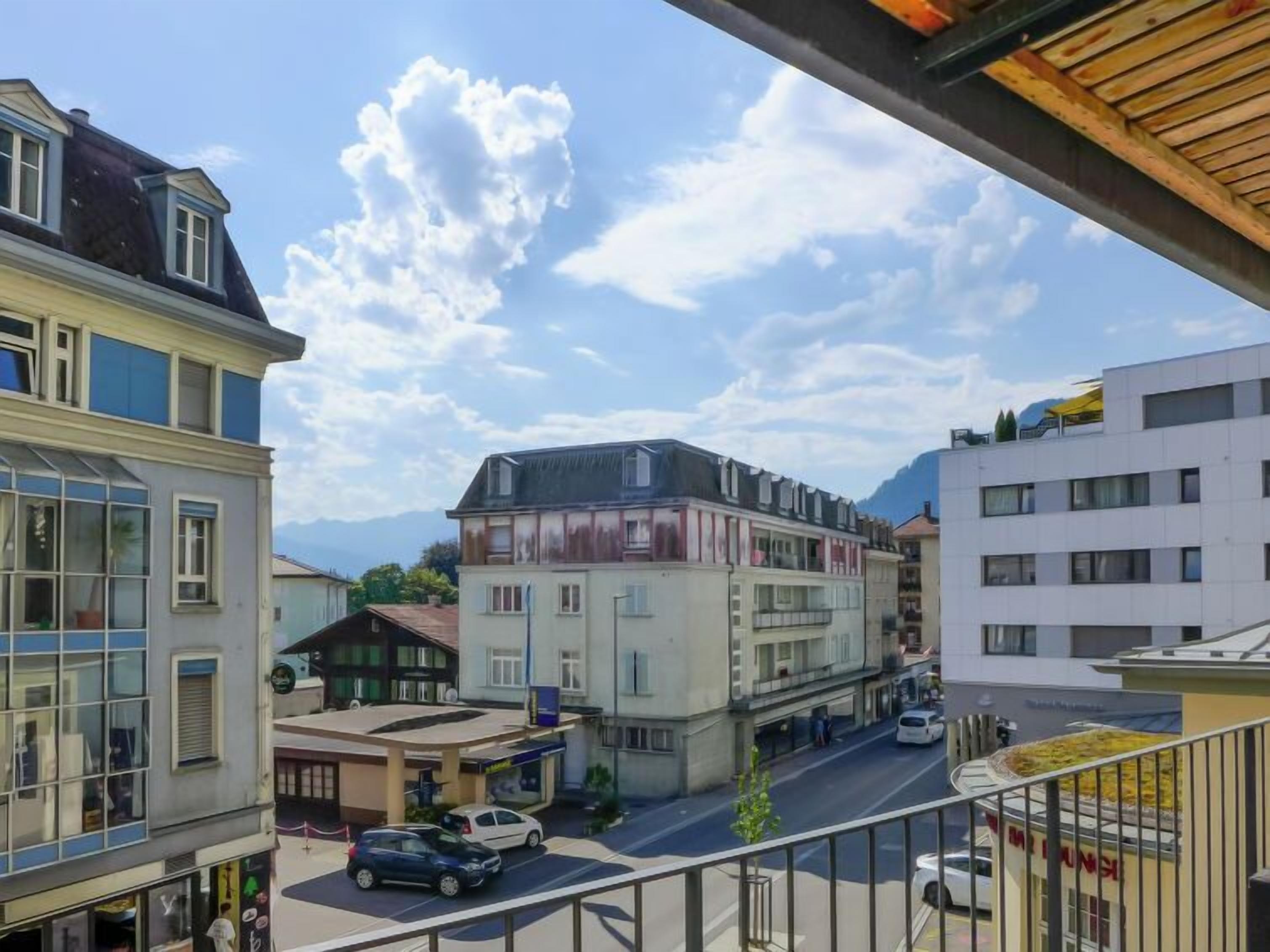 A street view with buildings, a clear sky, and a mountain in the background.