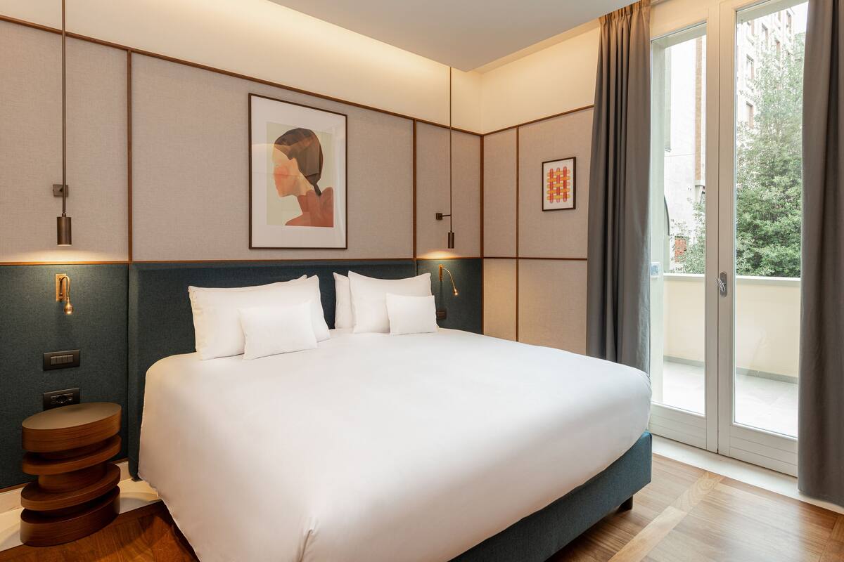 A large bed with white linens, a headboard, and a bedside table with a round wooden base.