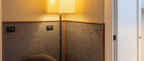 Una habitación de hotel moderna con un otoman negro redondo, una mesita blanca pequeña y una lámpara de pared.