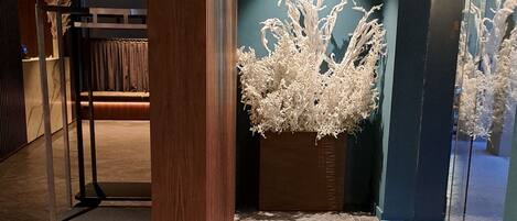 A hotel lobby with a herringbone-patterned floor, a large white decorative plant, and a wooden column.
