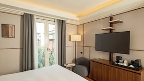 A hotel room with a bed, a TV, a desk with a coffee maker, and a view of a balcony. - Hotel Brun (Bologna)