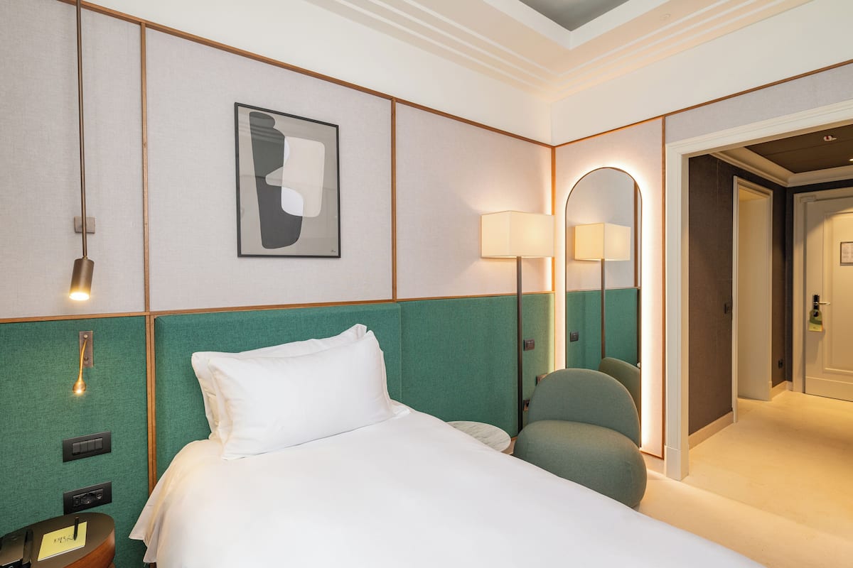 A hotel room with a bed, a desk with a lamp, a chair, and a mirror.