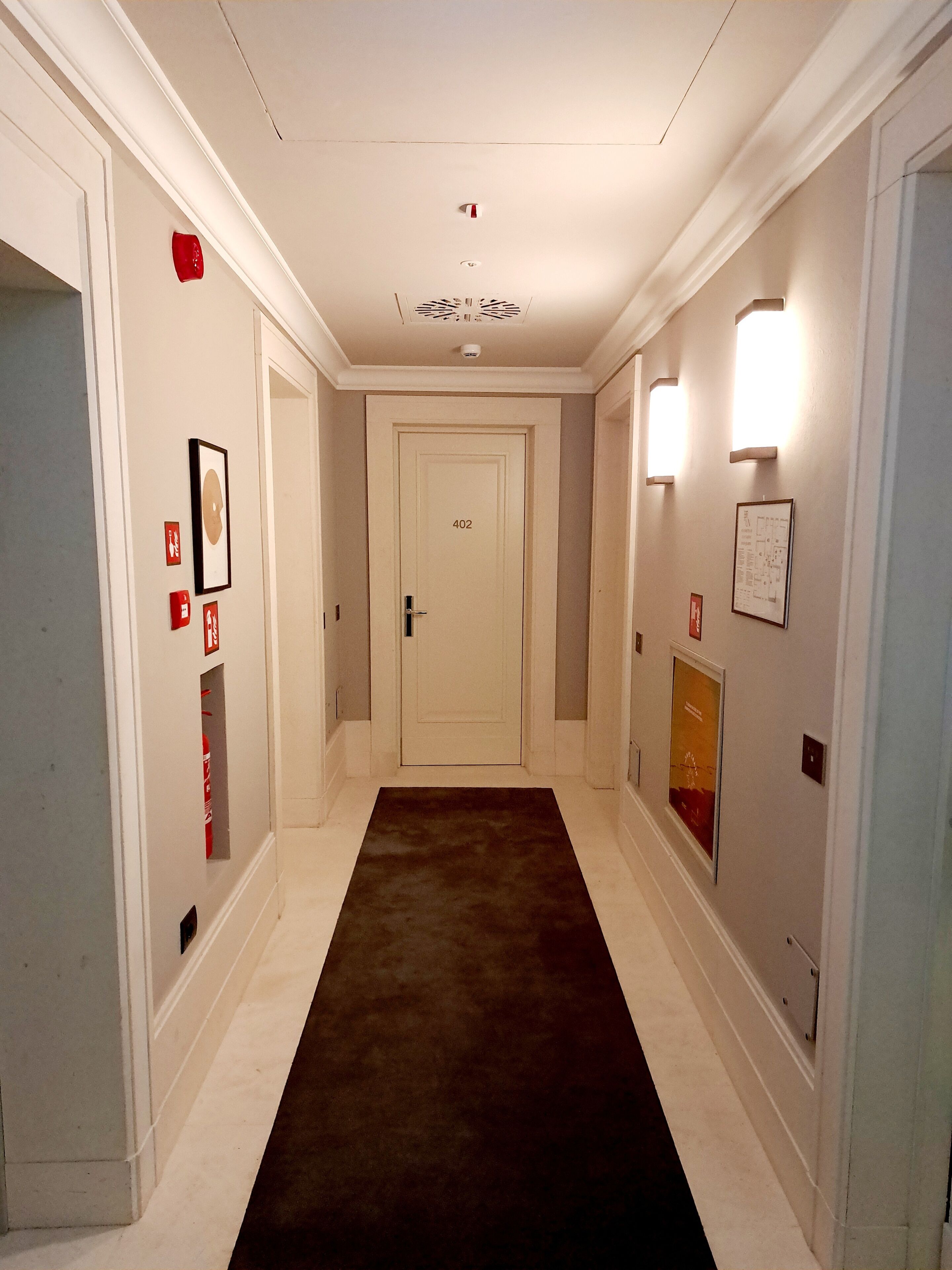 A hallway with a dark brown carpet, white walls, and a door marked with the number 402.