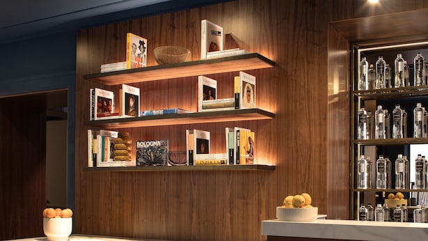A well-organized bar area with wooden shelves displaying books and bottles, a marble countertop, and a bowl of oranges. - Hotel Brun (Bologna)