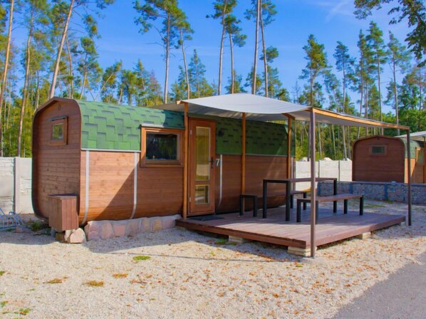 A small wooden cabin with a covered patio area, a door, and a window.