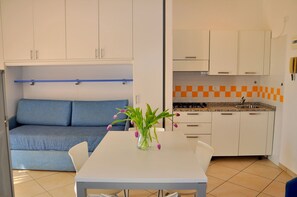 A compact kitchen with white cabinets, a blue sofa, and a dining table with a vase of flowers. - Flat in a Seafront Building With Swimming Pool (San Michele al Tagliamento)