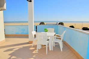 A balcony with a table and chairs, overlooking a beach. - Flat in a Seafront Building With Swimming Pool (San Michele al Tagliamento)