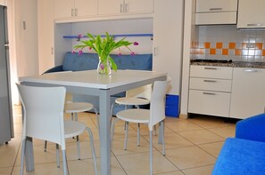 A compact kitchen with white cabinets, a blue bench, and a small dining table with chairs. - Flat in a Seafront Building With Swimming Pool (San Michele al Tagliamento)