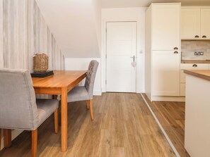 A compact kitchen with white cabinets, a wooden dining table, and a grey upholstered chair.