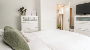 Un dormitorio con cama, cómoda, televisor y puerta que da a un baño.