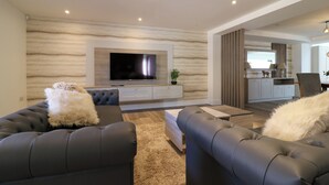 A modern living room with a large flat-screen TV, two black leather sofas, a wooden coffee table, and a beige shag rug. - Northumberland Luxury Stays - The Newland (Morpeth)