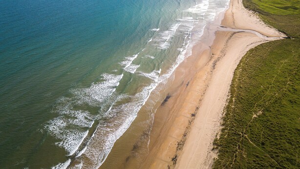 An aerial view of a beach with a long stretch of sandy shore and grassy areas. - Northumberland Luxury Stays - The Newland (Morpeth)