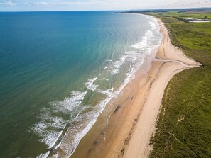 An aerial view of a beach with a long stretch of sandy shore and grassy areas. - Northumberland Luxury Stays - The Newland (Morpeth)