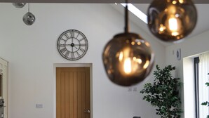 A modern dining area with a wooden door, a wall clock, pendant lights, and a potted plant. - Northumberland Luxury Stays - The Newland (Morpeth)