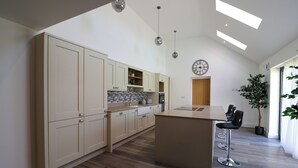 A modern kitchen with high ceilings and skylights, featuring light-colored cabinets, a central island, and bar stools. - Northumberland Luxury Stays - The Newland (Morpeth)
