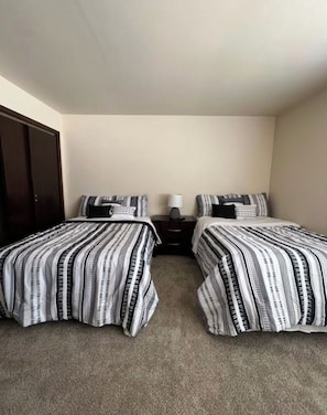 A room with two beds, each with striped bedding, a nightstand with a lamp, and a dark wardrobe.