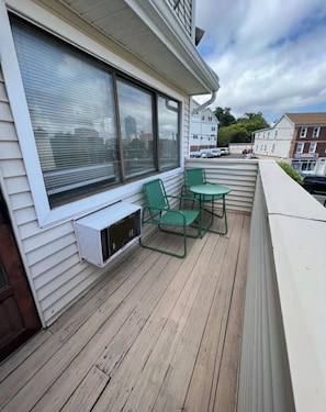 A covered outdoor area with a wooden deck, two green chairs, and a small table.