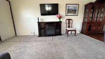 A living room with a flat-screen TV mounted on the wall, a wooden cabinet, a chair, and a carpeted floor.