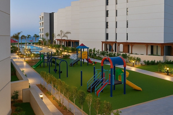 A playground with slides and climbing structures, surrounded by a landscaped area with trees and a pool in the background.