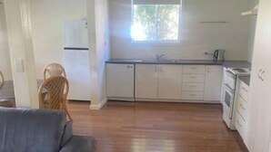 A spacious living area with a grey sofa, wooden flooring, and a kitchen with white cabinets and a window. - Golden street cottage

 (West Wyalong)