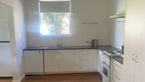 A kitchen with white cabinets, a window, and a wooden floor. - Golden street cottage

 (West Wyalong)