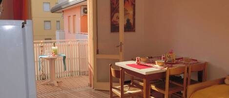 A room with a balcony, a dining table with chairs, a bed, and a refrigerator.
