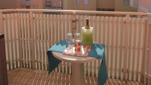 Un balcón con una mesa lista para dos personas, una botella de bebida y un pequeño florero.