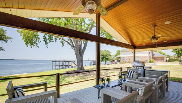 Een terras buiten met houten meubels, een barbecue en uitzicht op het water.