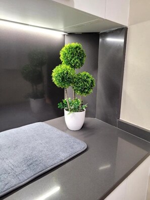A corner of a room with a grey mat, a white planter with a small tree, and a metallic wall.